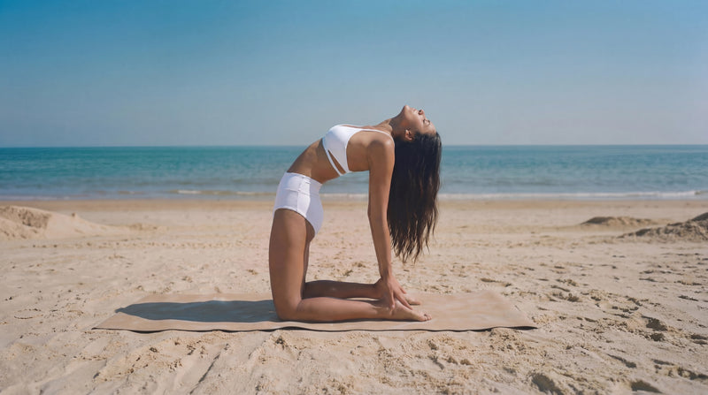 Woman practicing yoga on a beach with clear blue sky and ocean.