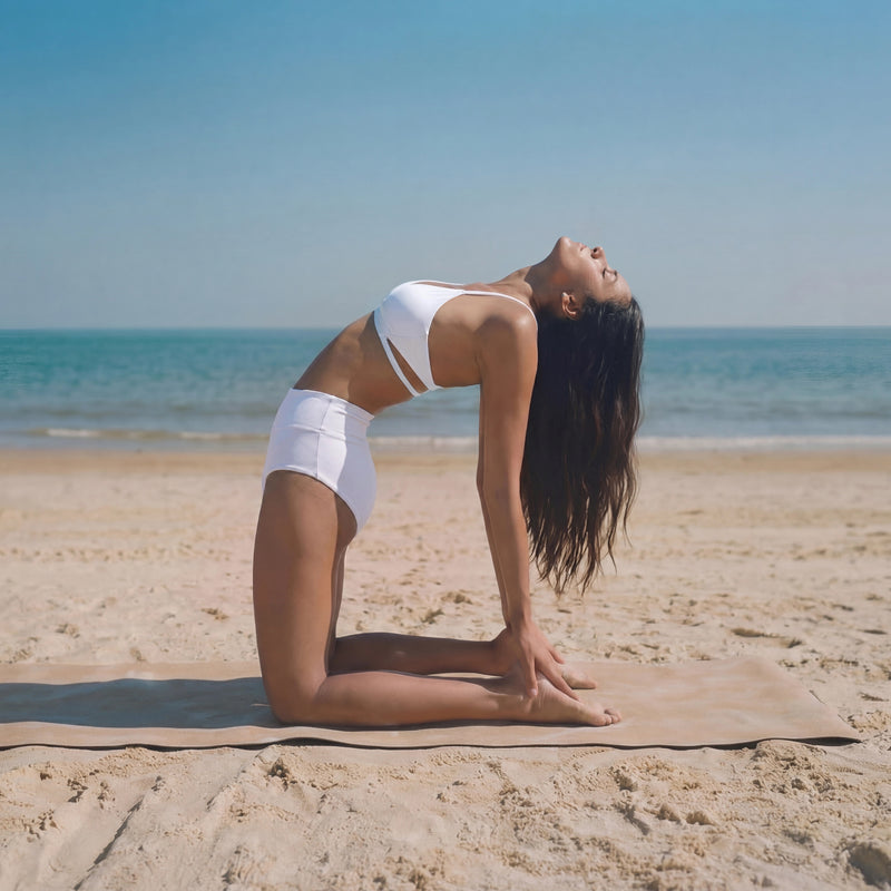 Woman practicing yoga on a beach with clear blue sky and ocean.