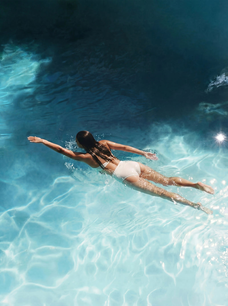 Person floating in clear blue water with sunlight filtering through